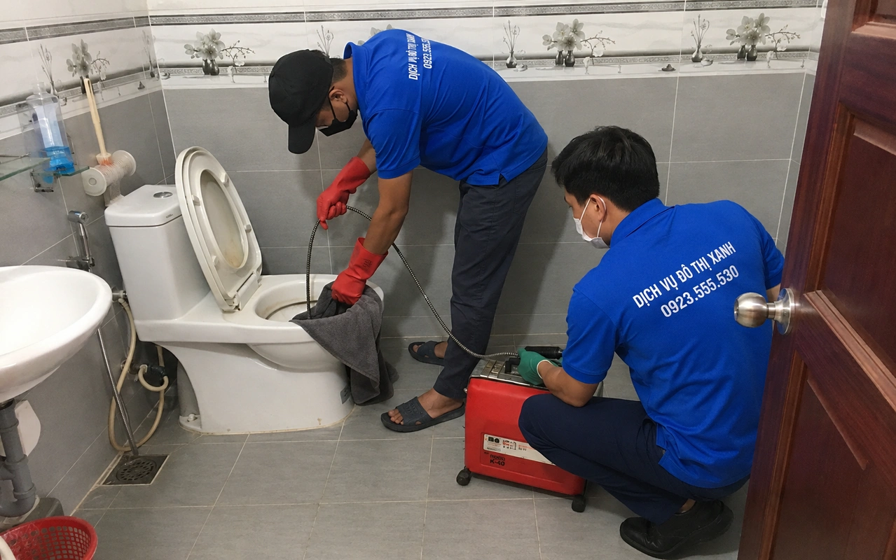 Hai nhân viên xử lý bồn cầu bằng thiết bị