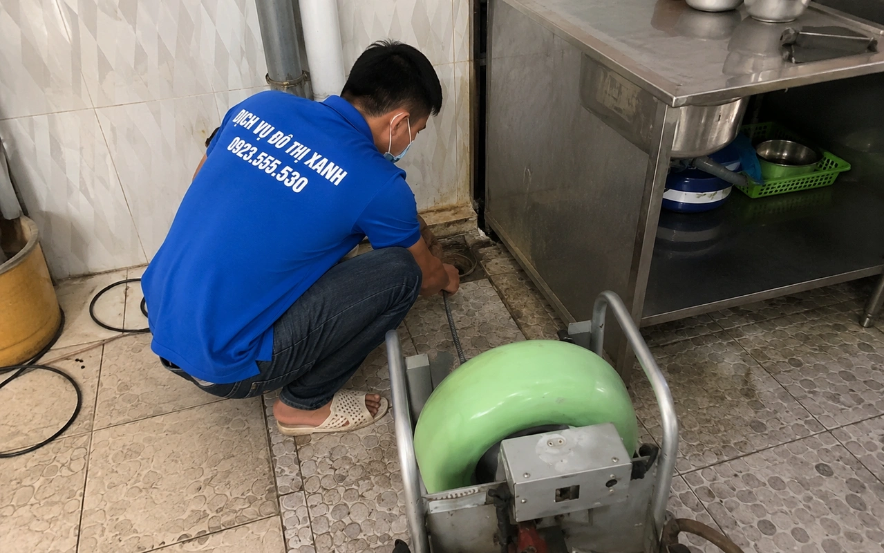 Nhân viên sử dụng máy lò xo xử lý đường thoát nước cạnh chậu bếp